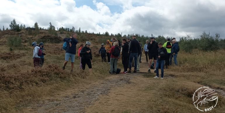 Účastníci exkurze v bundách a cyklistických helmách se rozhlížejí po odlesněné dopadové ploše.